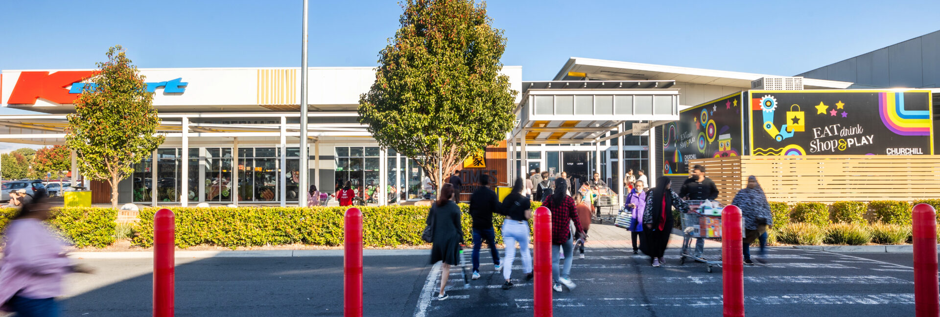 Families and visitors entering Churchill Centre Kilburn surrounded by shops and vibrant murals.